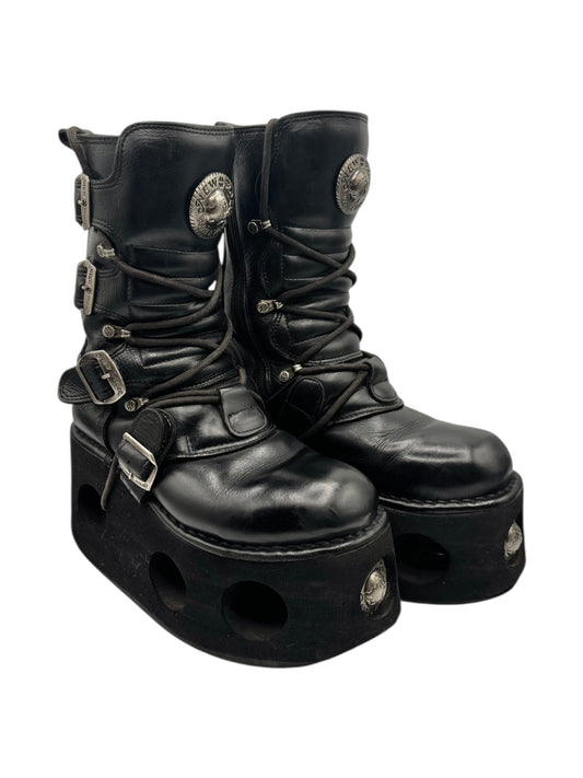 Black platform leather lace-up boots with front straps, buckles, and metal emblem patches