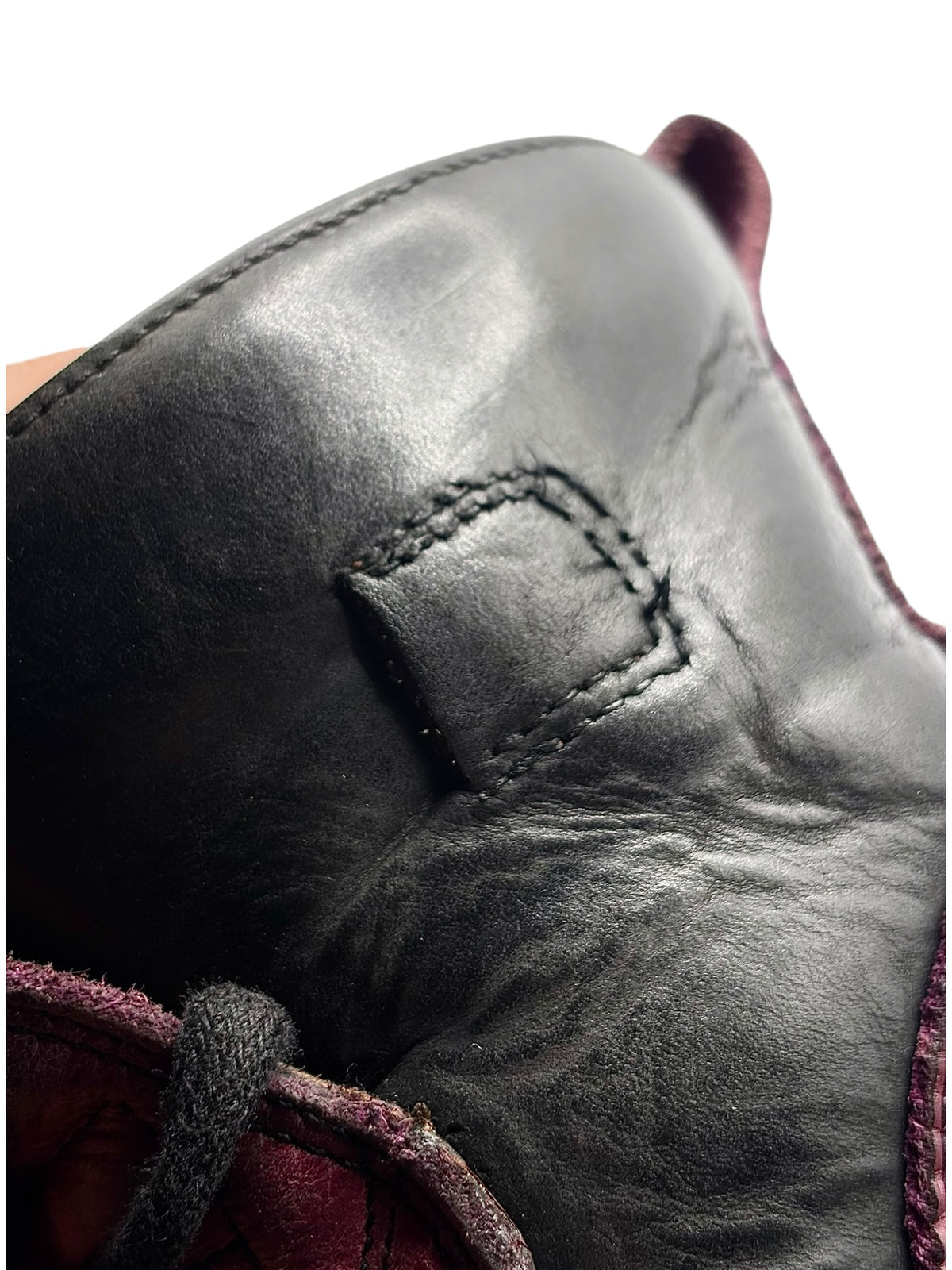 Black leather heel panel close-up with stitched square seam and worn texture