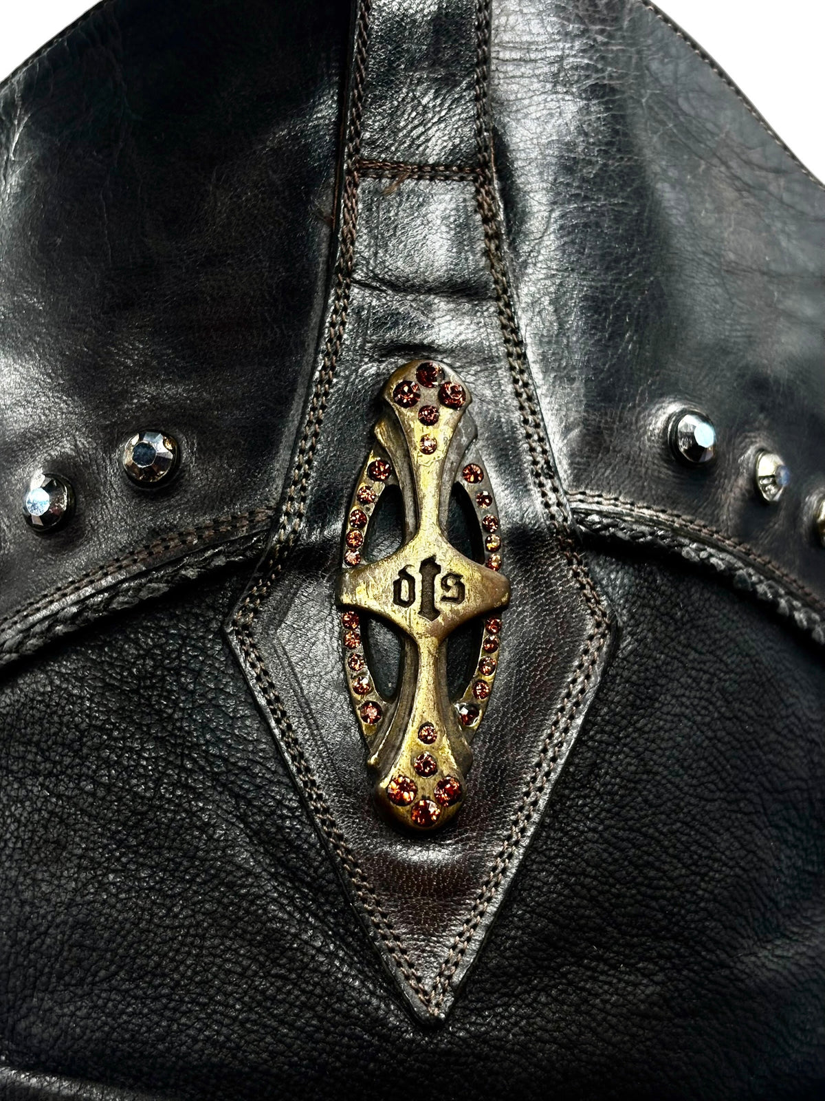 Vintage knee-high leather boots close-up with jeweled V medallion and metal studs