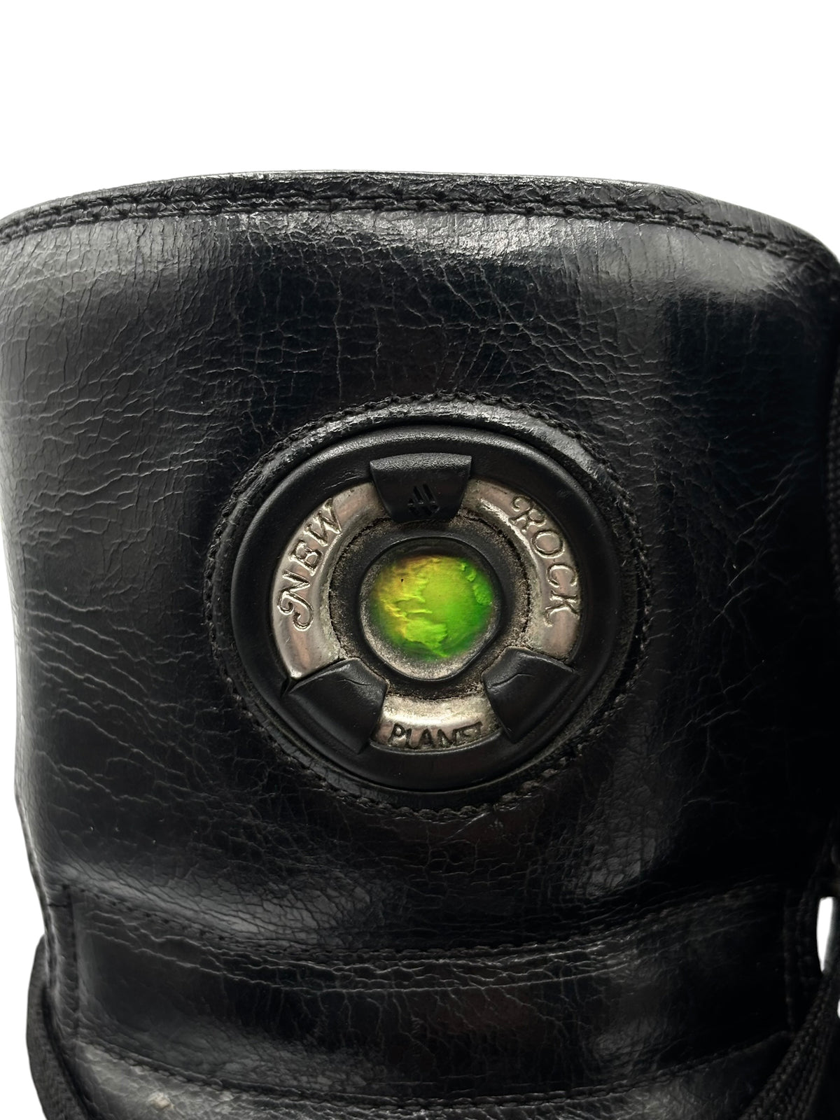 Black leather boot cuff close-up with circular emblem and green center