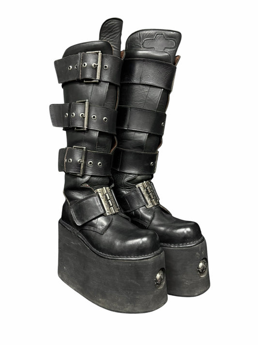 Angled pair view of black knee-high platform boots with stacked straps and metal buckles.