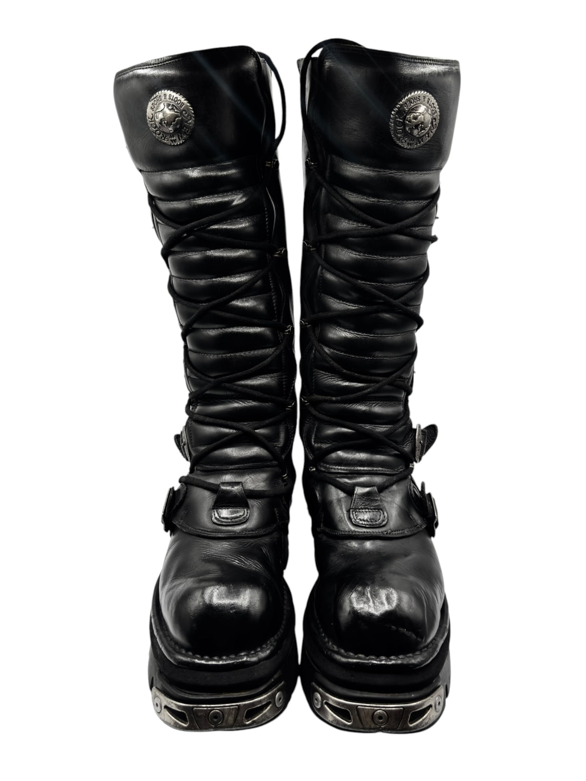 Knee-high lace-up boots with round emblem, buckled straps, and rugged outsole