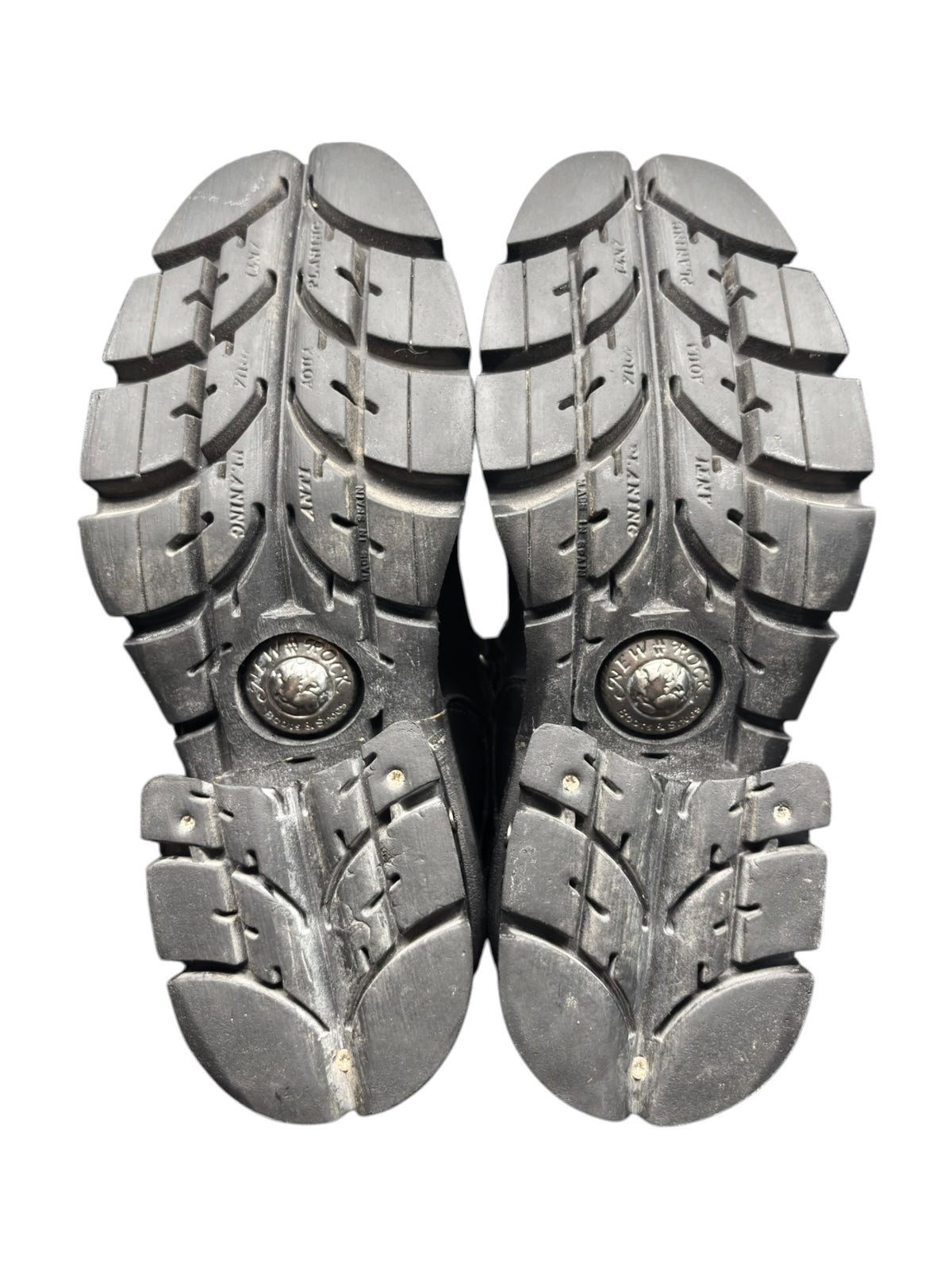 Pair of black boot outsoles with rugged tread and embossed circular logo badges.