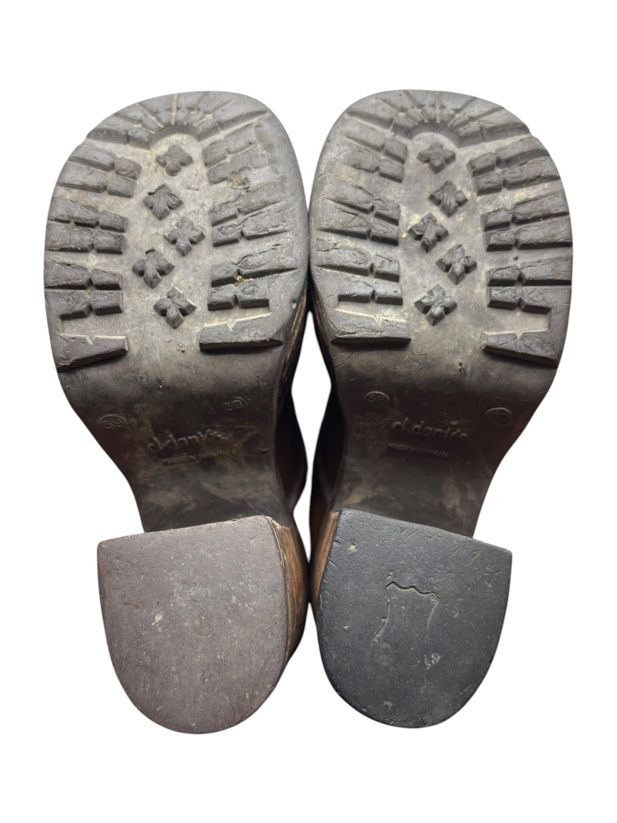 Outsoles of brown mid-calf boots with tread pattern and stacked heel bases.