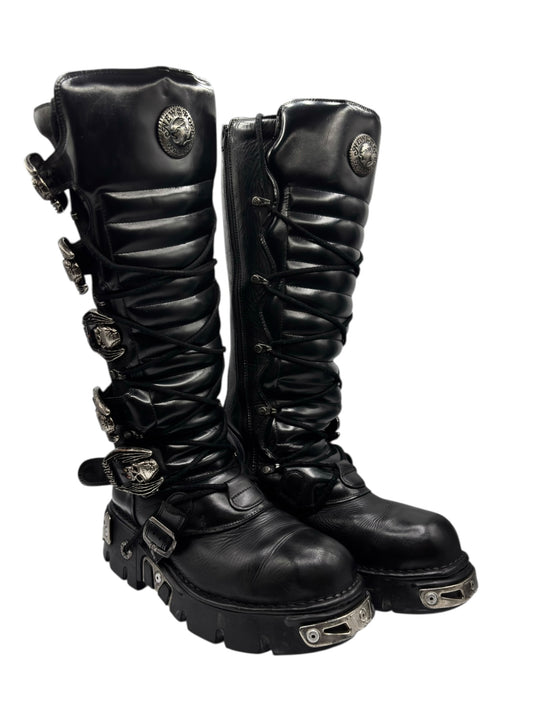 Knee-high black leather lace-up boots with side buckles and chunky metal-strap accents