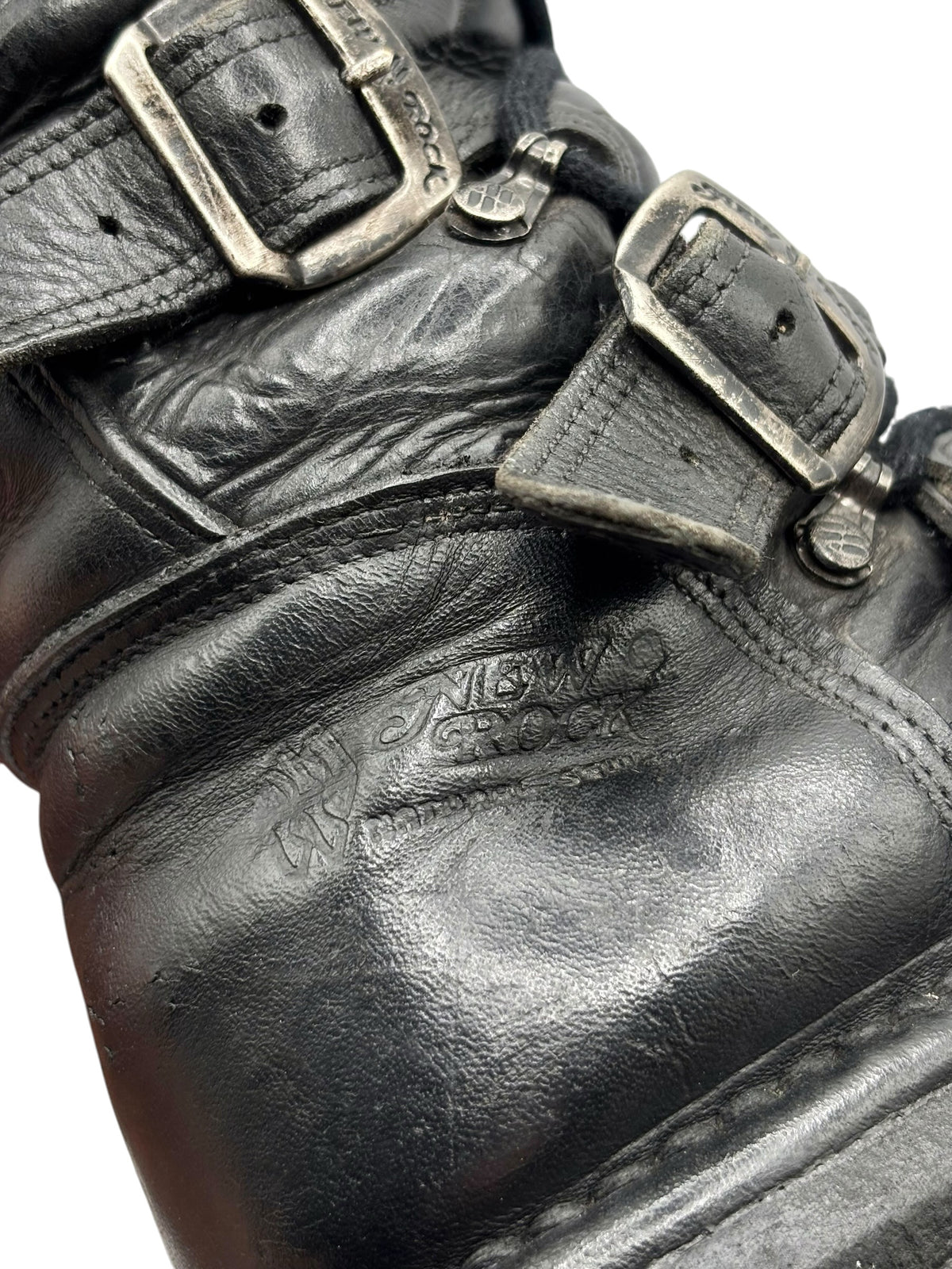 Close-up of black leather boot with stitched panel and metal buckles on strap