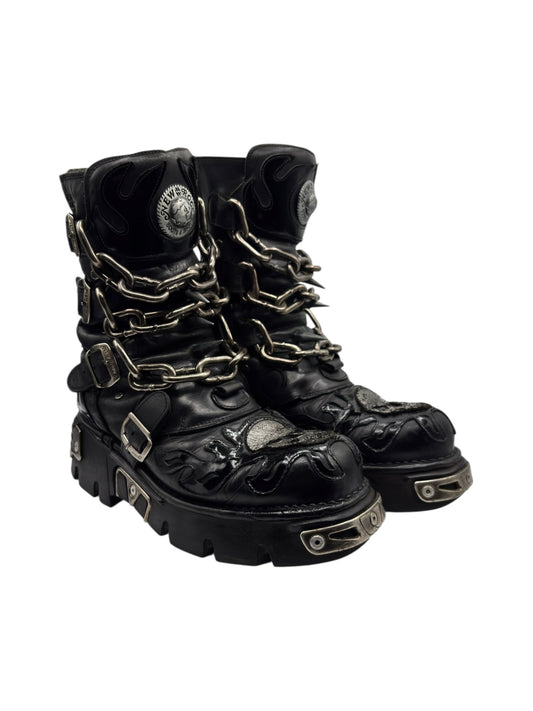Three-quarter view of black leather combat boots with gold chain and rugged platform sole