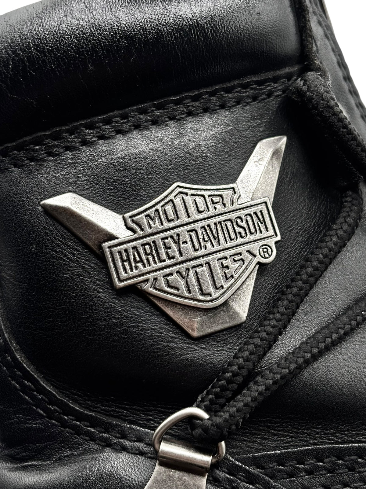 Close-up of Harley-Davidson wing logo on black leather boot near lace grommet