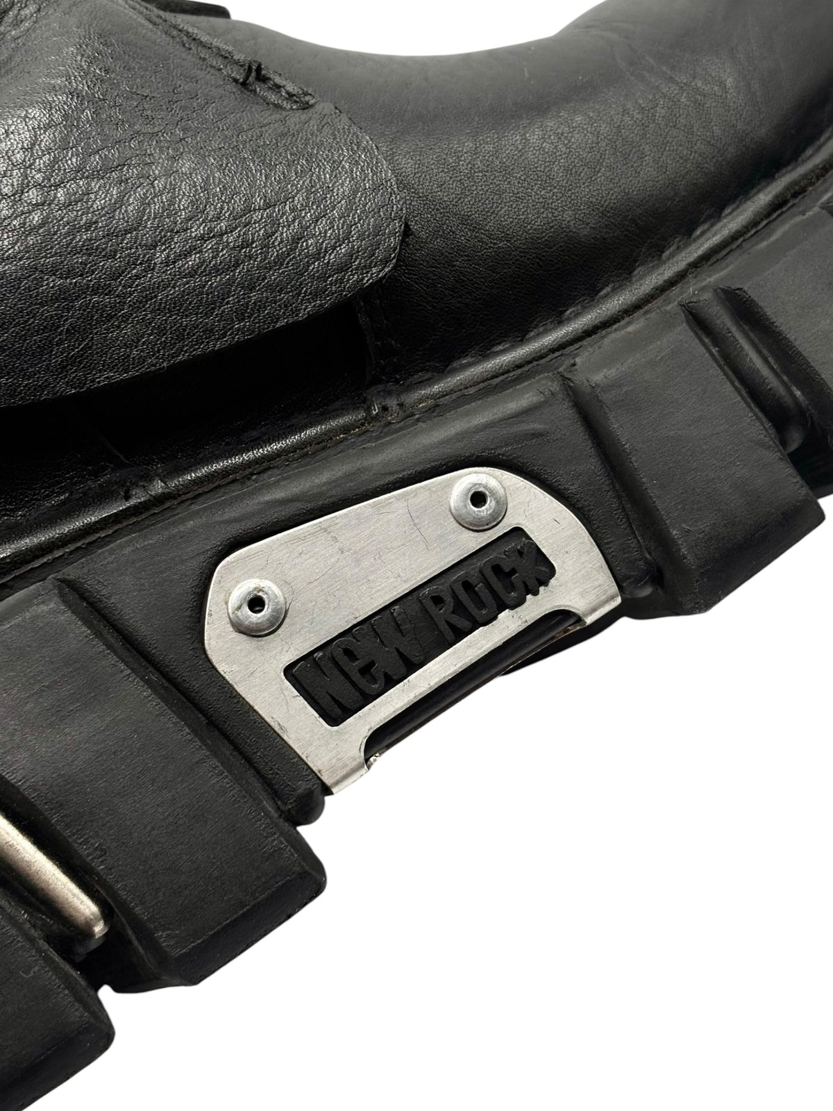 Close-up of black boot strap with silver “NEVER ROCK” metal nameplate