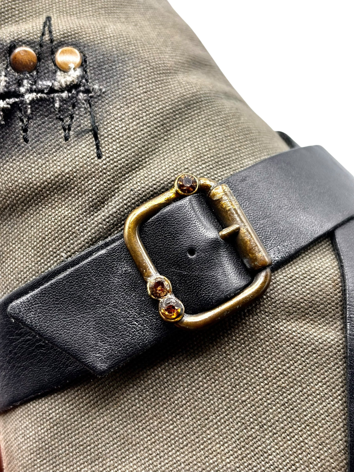 Knee-high boot close-up: black leather buckle strap on olive canvas upper