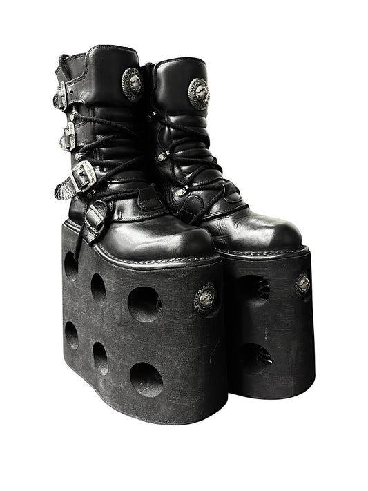 Black platform boots with cutout heel sides, buckle straps, and round emblem patches