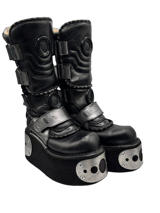 Black platform boots with side buckles, layered straps, and silver metal toe guards