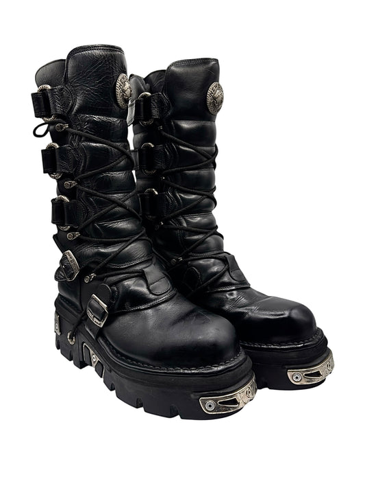 Black knee-high leather boots with lace-up and side straps, buckle details, chunky tread.