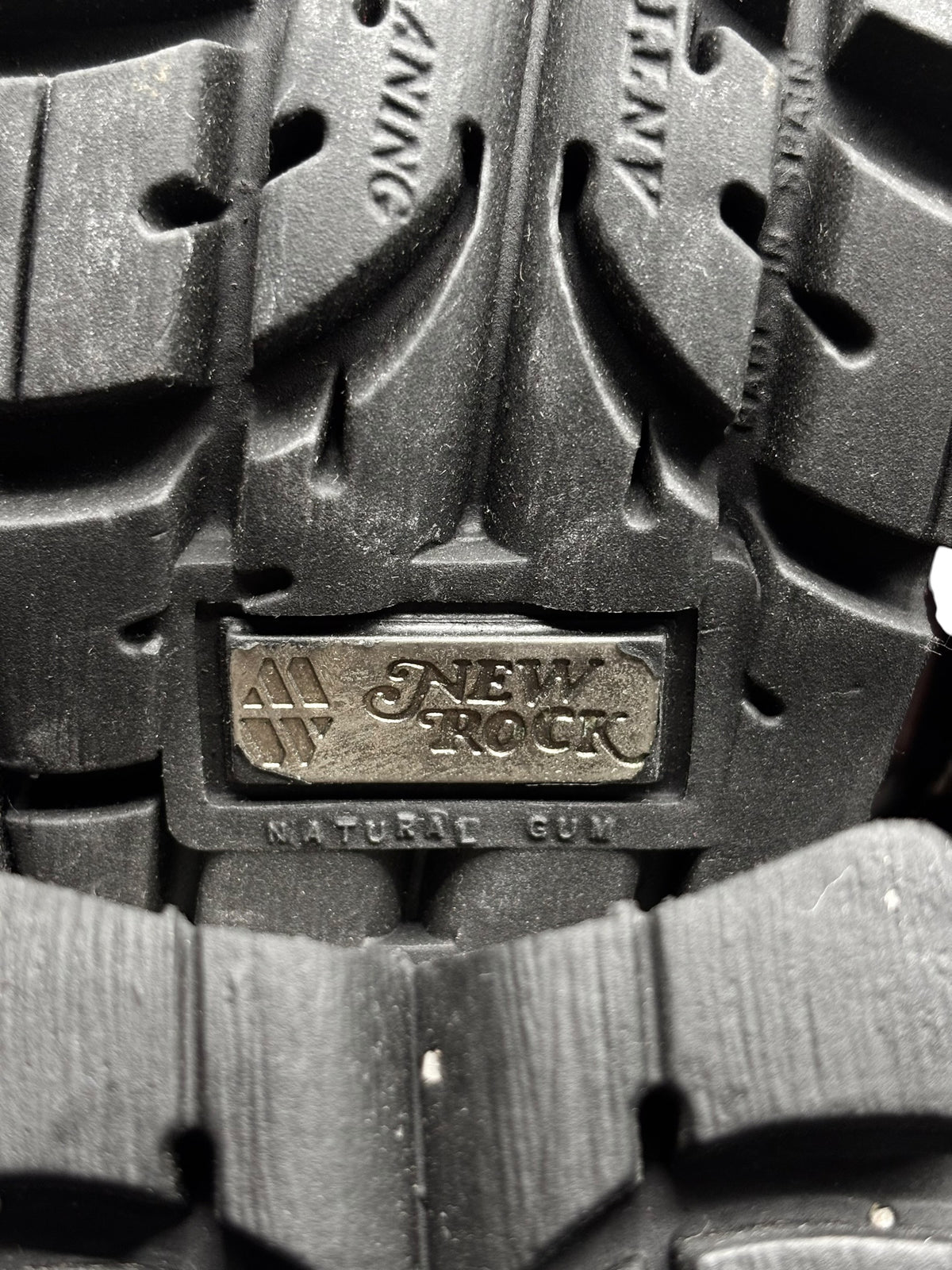 Shoe sole close-up with rugged tread and embossed brand logo on outsole.