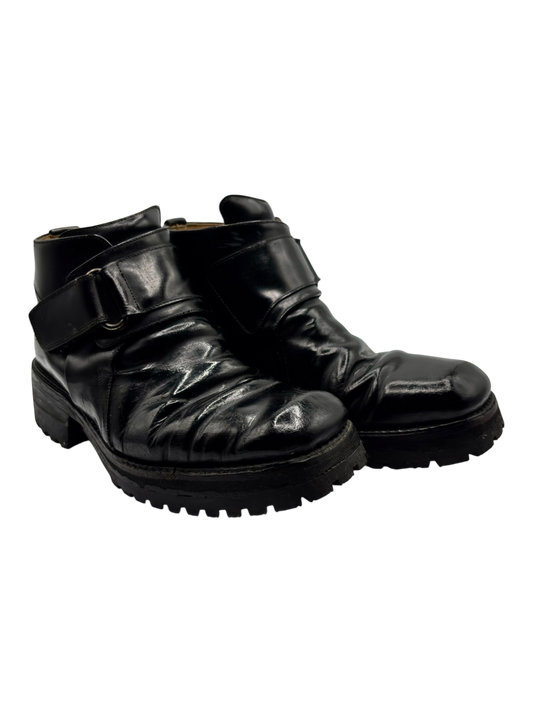 Black leather ankle boots with buckle strap, glossy finish, and chunky lug sole.