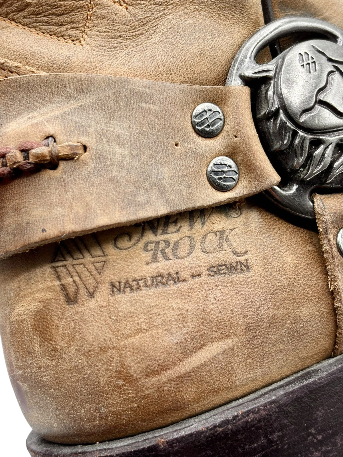 Beige boot strap with metal concho and small round stud accents near buckle