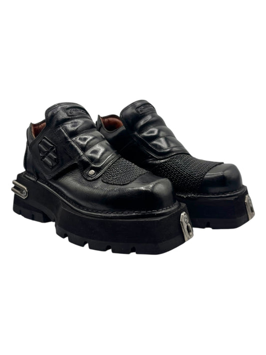 Black platform ankle boots angled view showing overlapping straps and metal bars