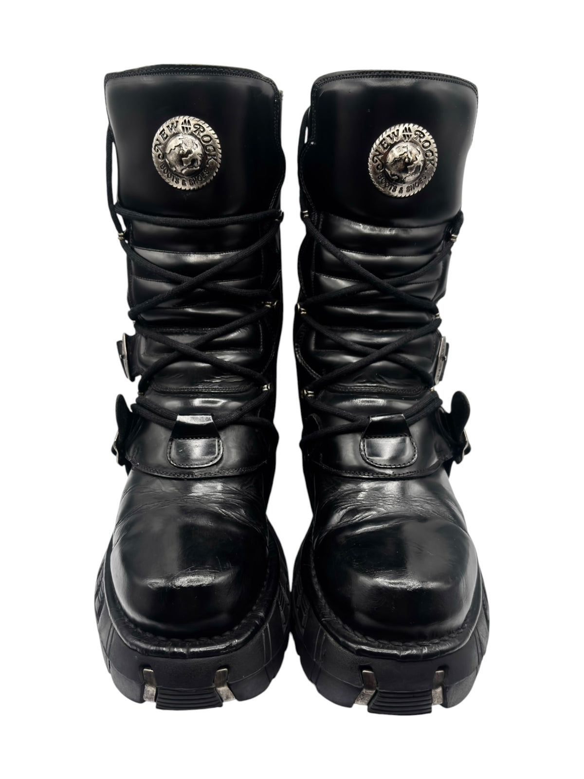 Black platform boots front view with lace-up design, buckled straps, and round logo patch.