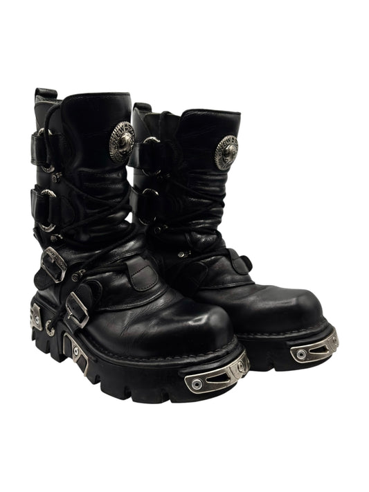 Black mid-calf leather boots angled view with front buckles and chunky lug sole.