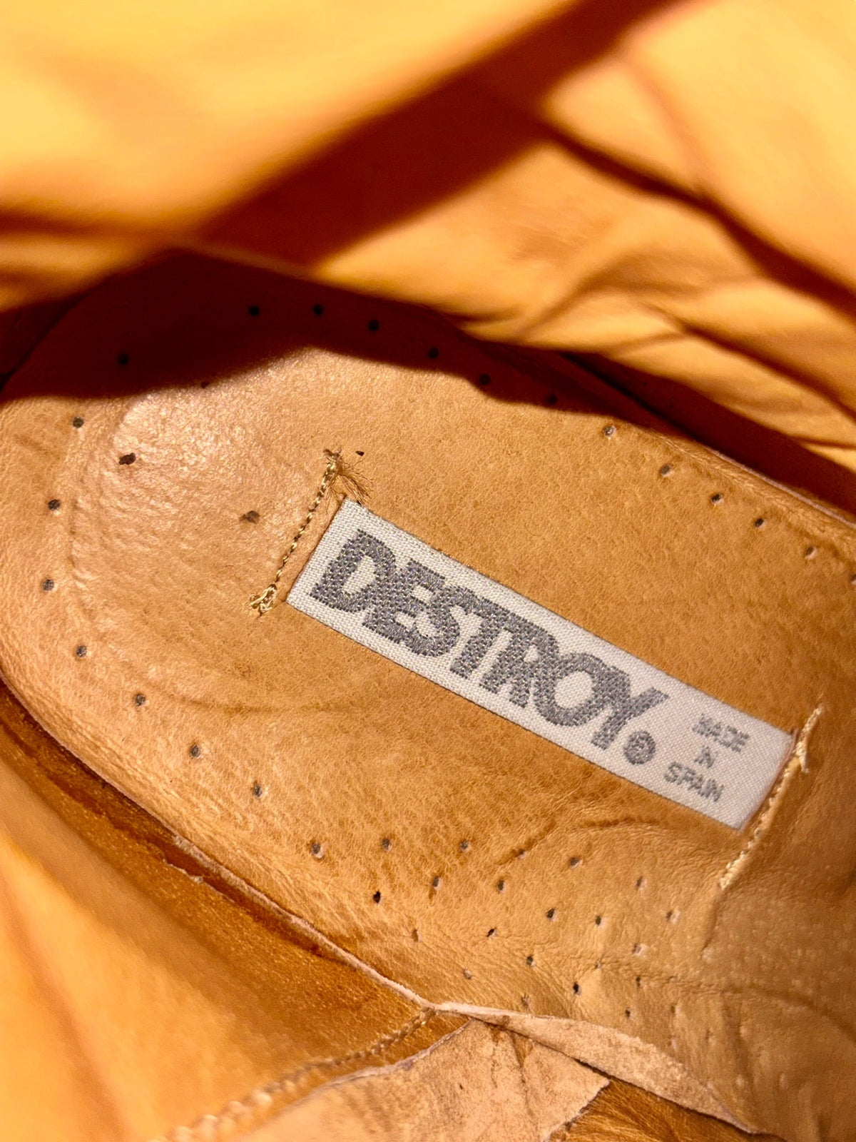 Close-up of brown boot leather with stitched label and small punched holes.