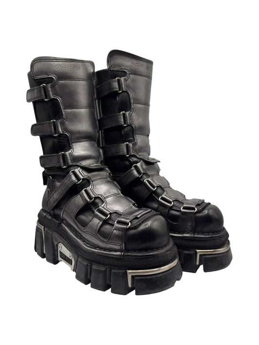 Knee-high dark leather boots with chunky platform heel, multiple buckles, and lug sole