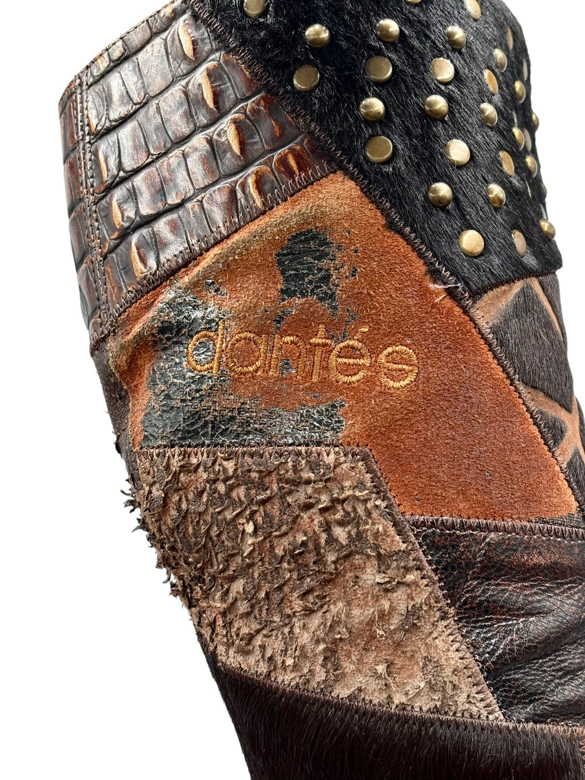 Close-up of patchwork leather boot with studs and “El Dantes” embossed logo.