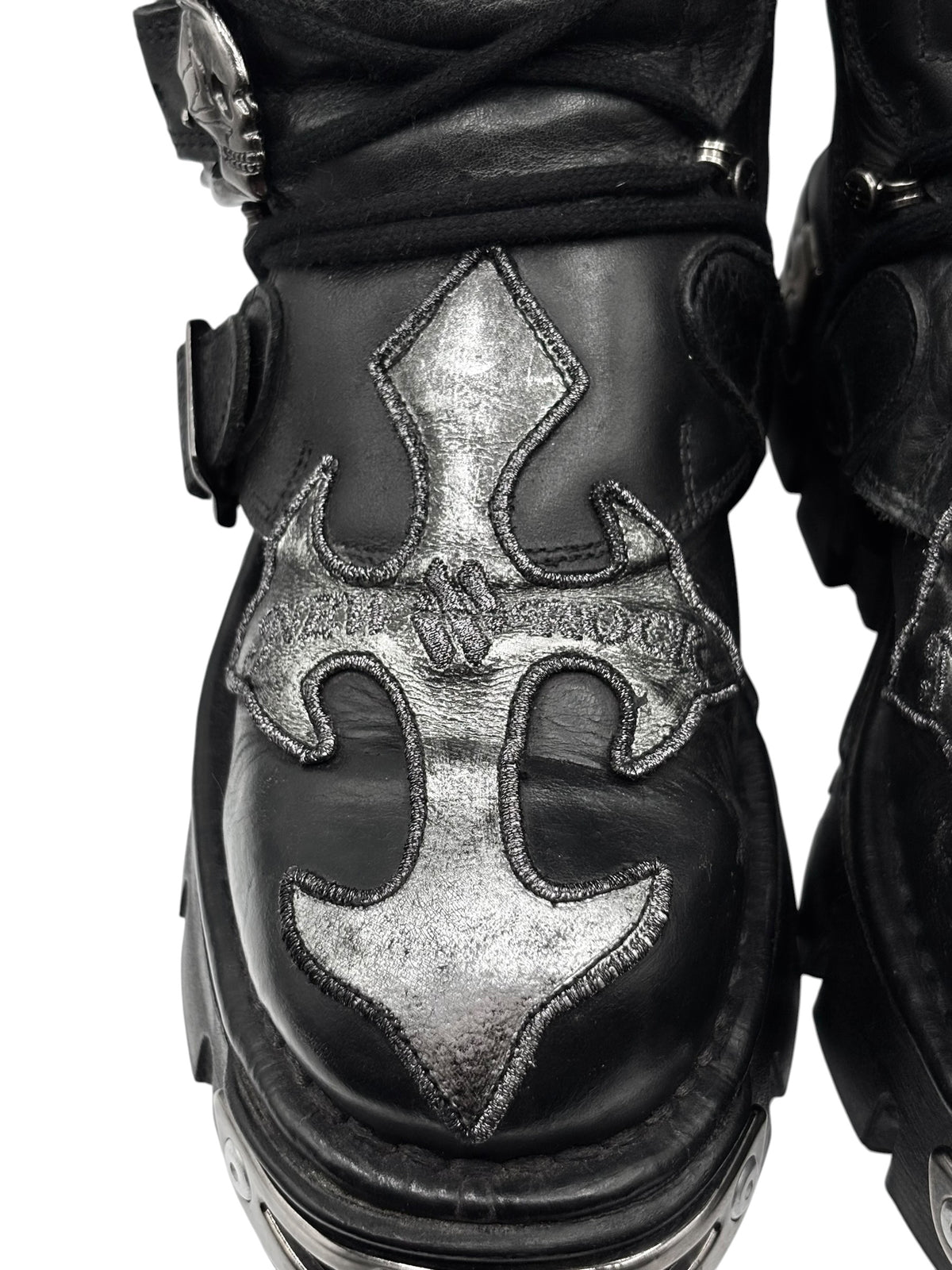 Close-up of black boot side panel with silver decorative emblem and stitching