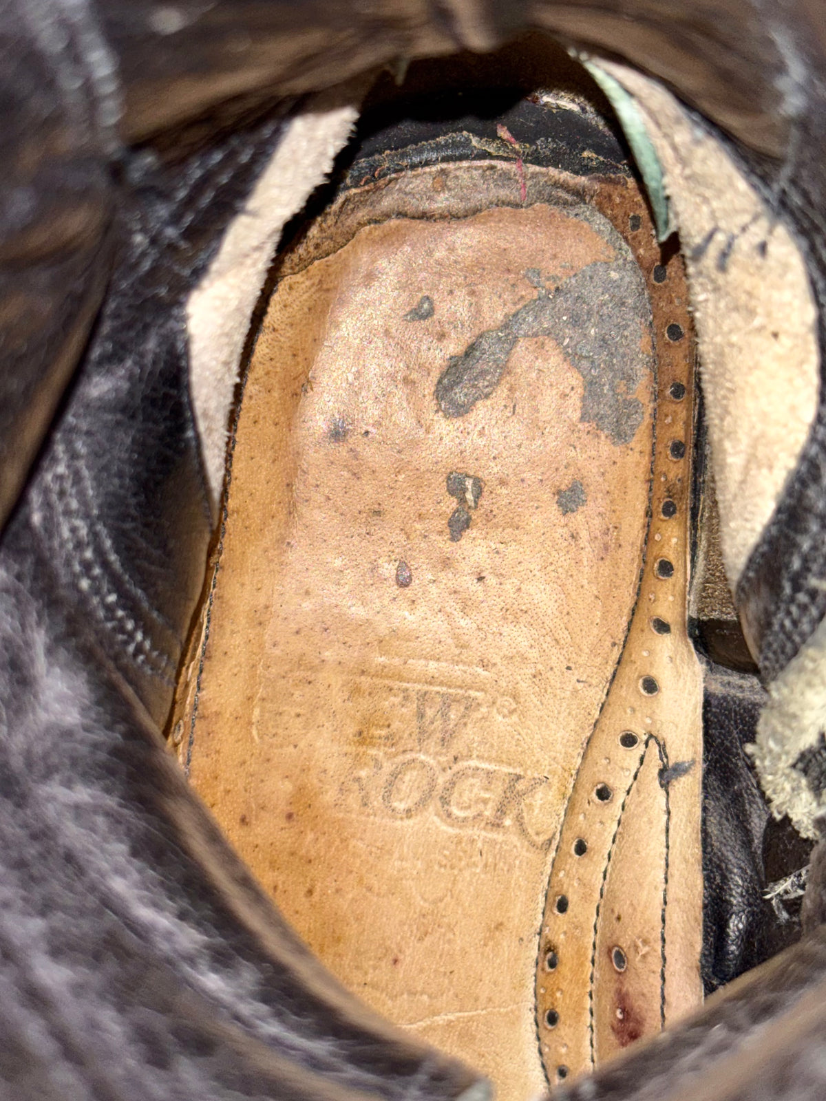 Boot interior insole close-up with tan leather and visible stitching and embossed logo.