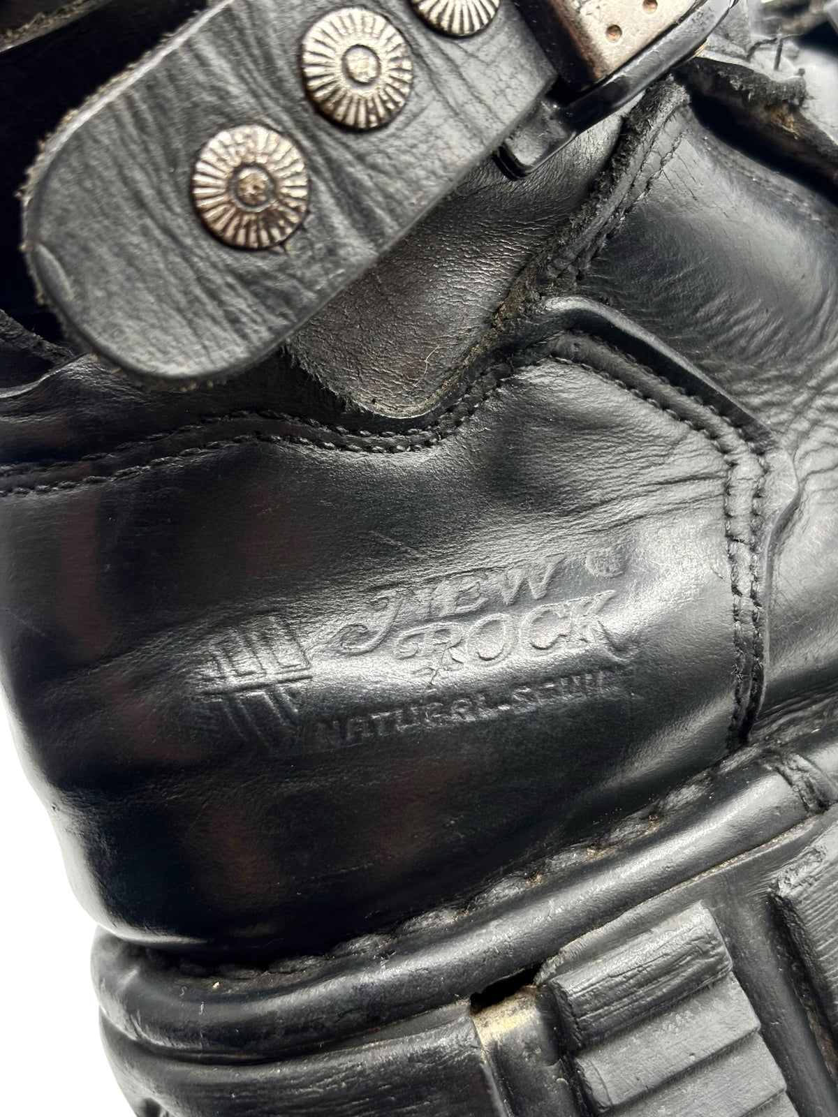 Close-up of black leather boot toe with embossed branding and studded panel