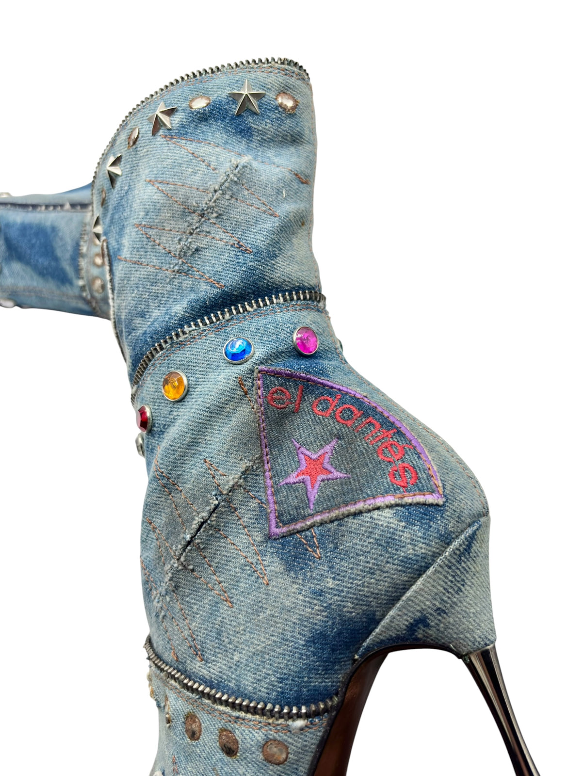 Denim boot ankle area with zipper, studs, and el dantes patch on blue fabric.