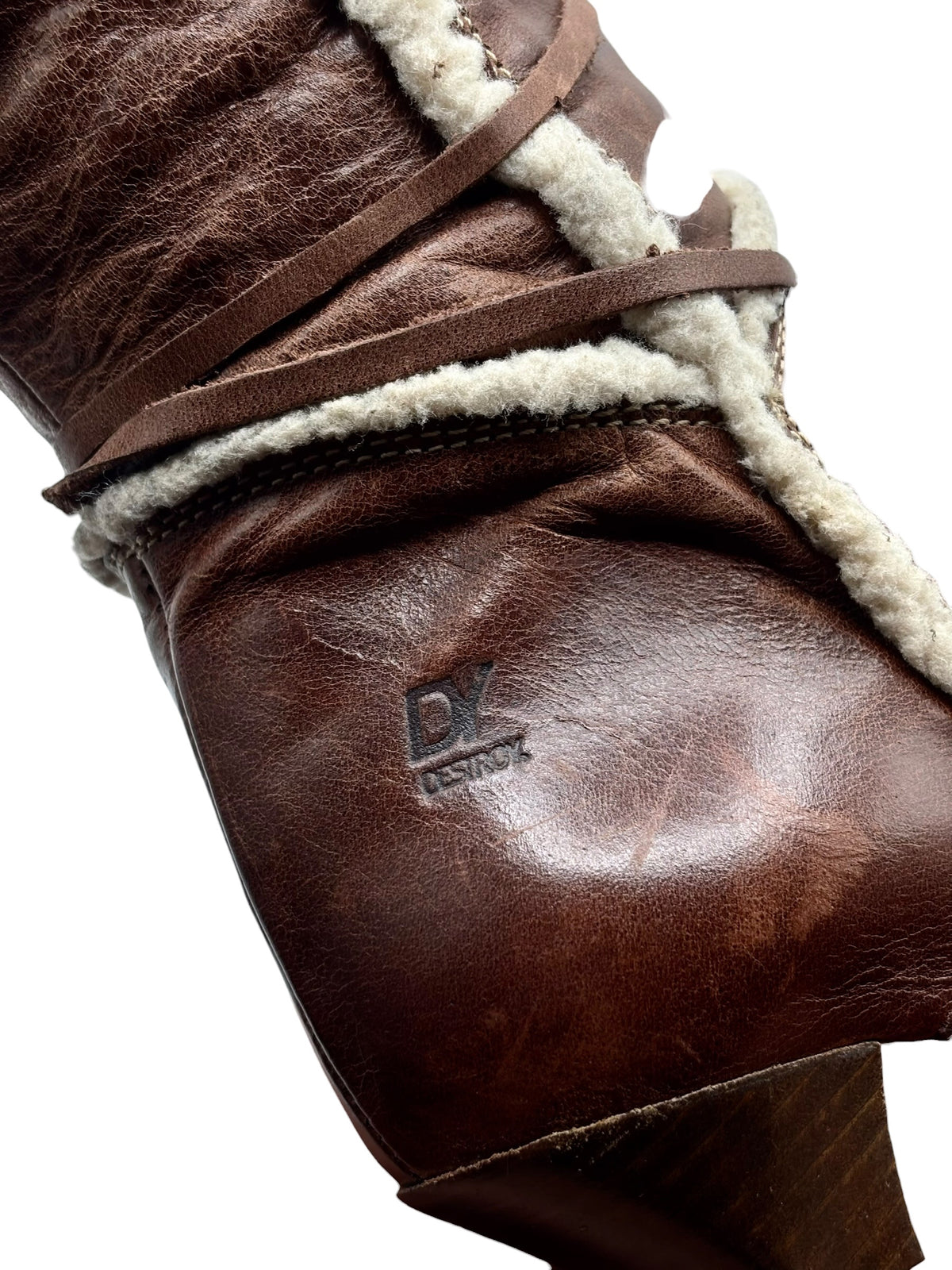 Close-up of brown leather boot with embossed logo and cream sherpa trim.