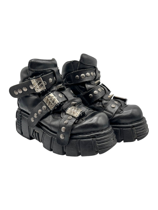 Black studded platform boots with crisscross straps, metal eyelets, and chunky sole.